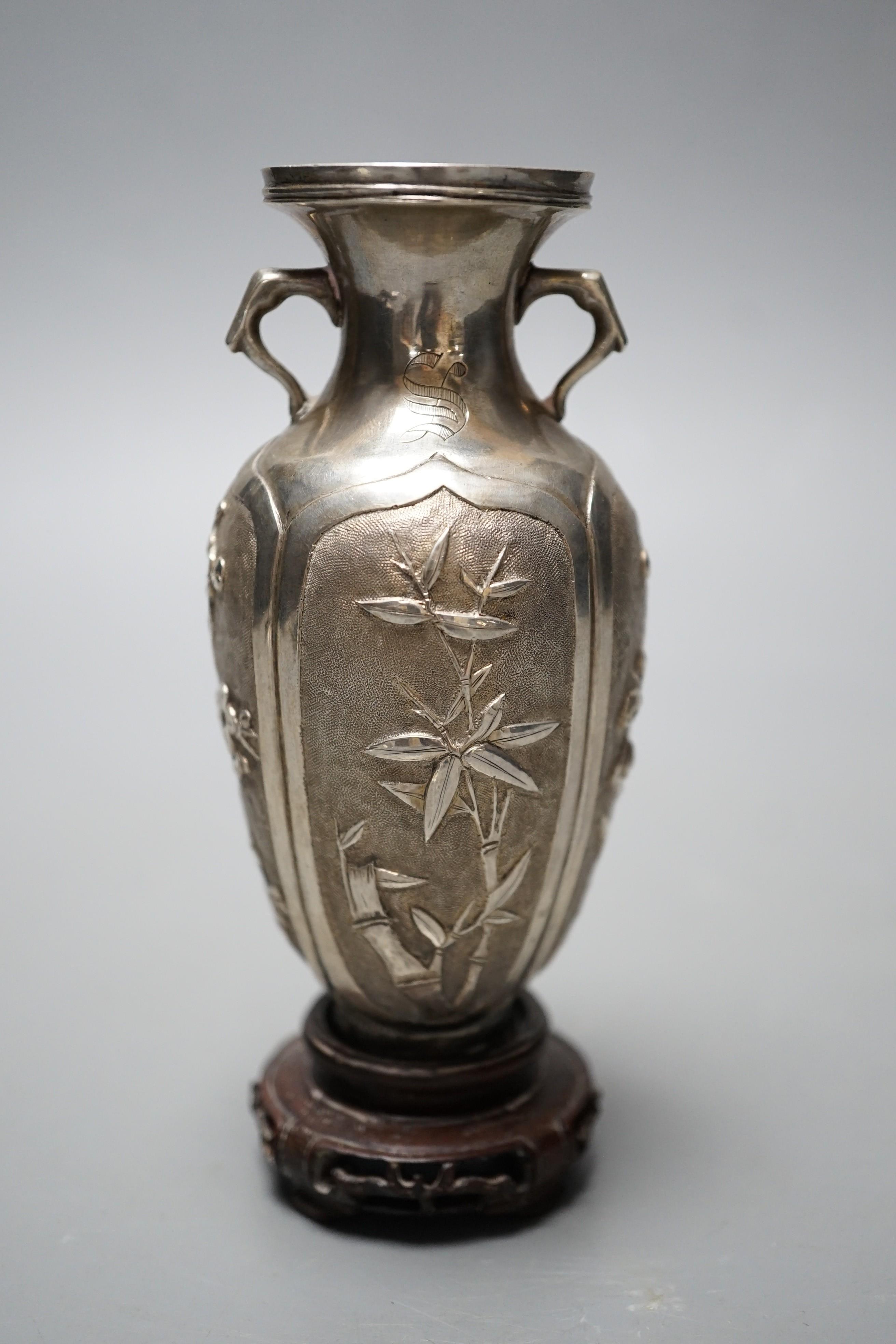 A late 19th/early 20th century Chinese Export white metal two handled vase, decorated with bamboo, peonies and prunus, on hardwood stand with white metal wing nut signed Zee Wo, vase 12cm.